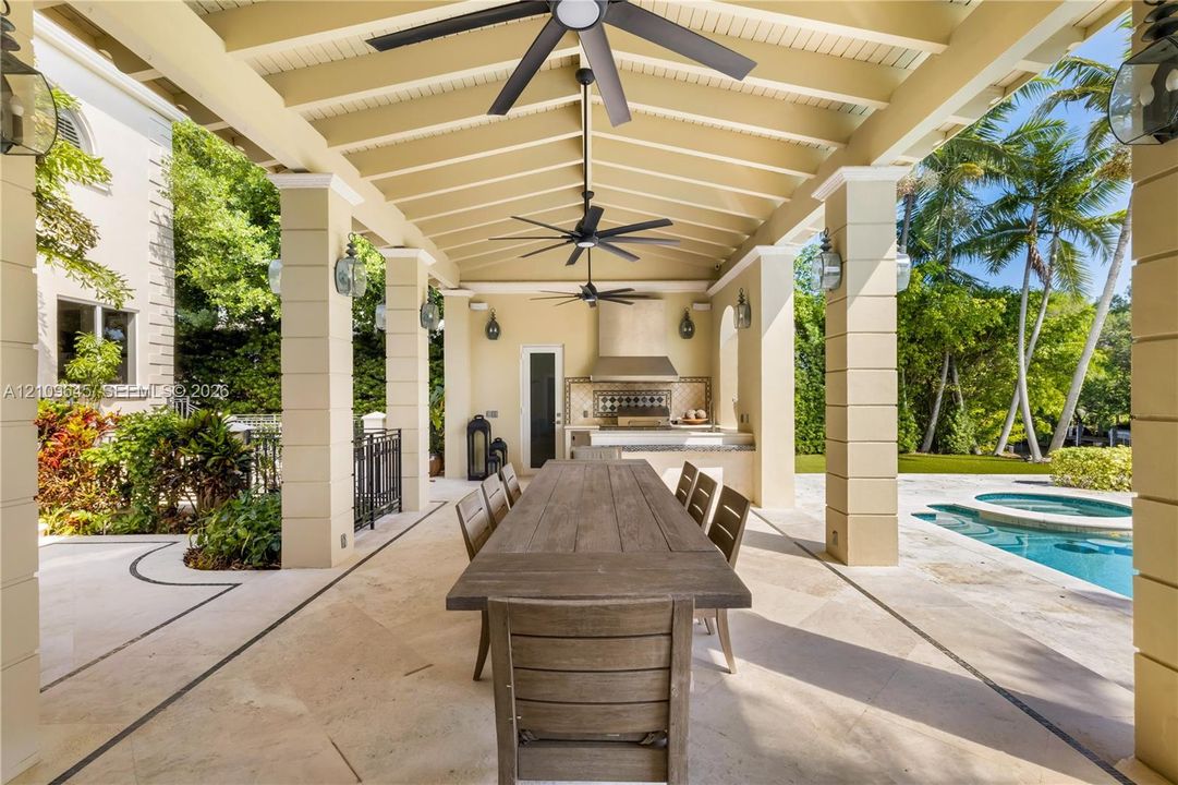 Covered outdoor terrace featuring a built-in kitchen, stone-tile flooring, decorative masonry columns, and recessed ceiling fans