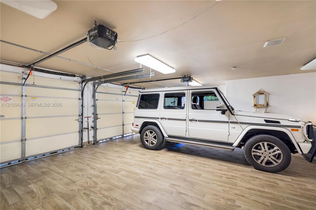 Garage featuring wood-finish flooring, dual motorized garage door openers, and rectangular LED light fixtures