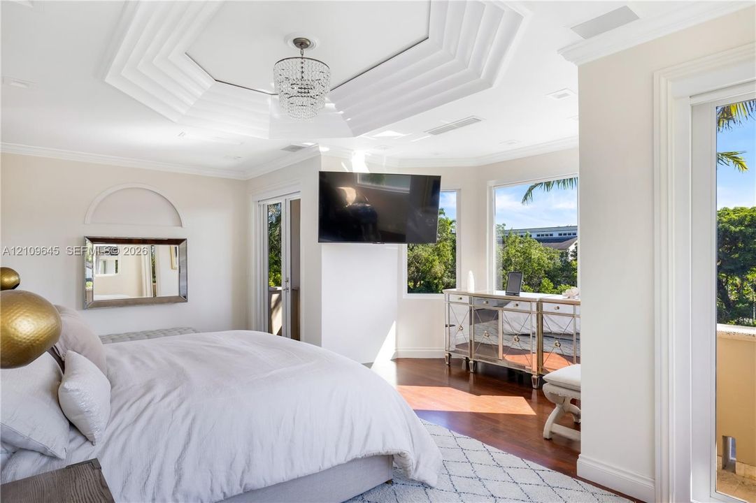 Octagonal tray ceiling featuring crown molding and a crystal chandelier, wood-finish flooring, and large windows with exterior foliage