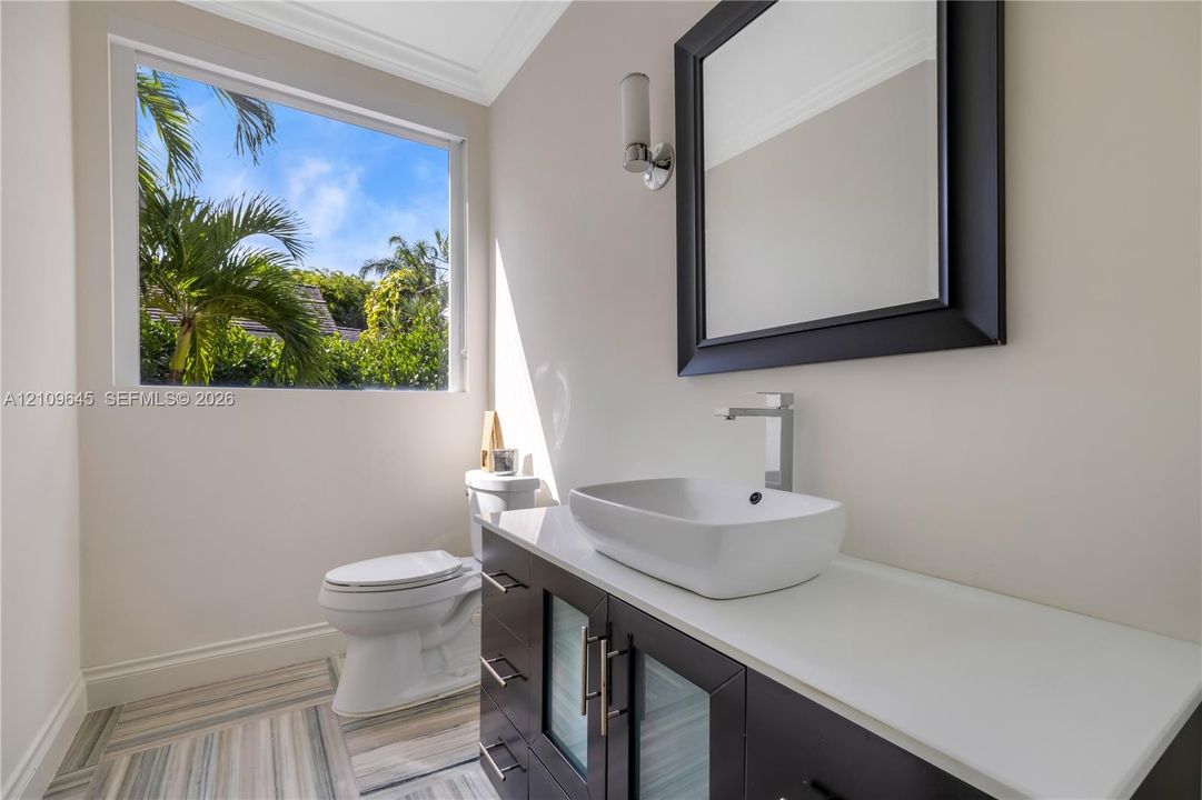 Modern vanity featuring a stone countertop, vessel sink, and metallic hardware, complemented by patterned tile flooring and a wall-mounted light fixture
