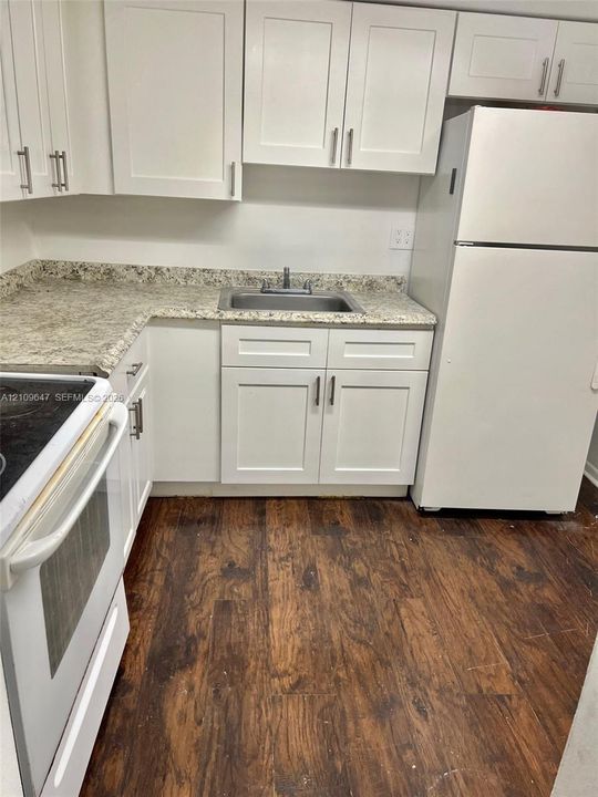 Kitchen featuring white shaker-style cabinetry, stone-finish countertops, stainless steel sink, and wood-finish flooring
