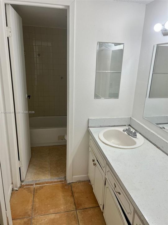 Bathroom vanity featuring a light-toned countertop with an integrated basin, white cabinetry, a wall-mounted mirror, and ceramic tile flooring