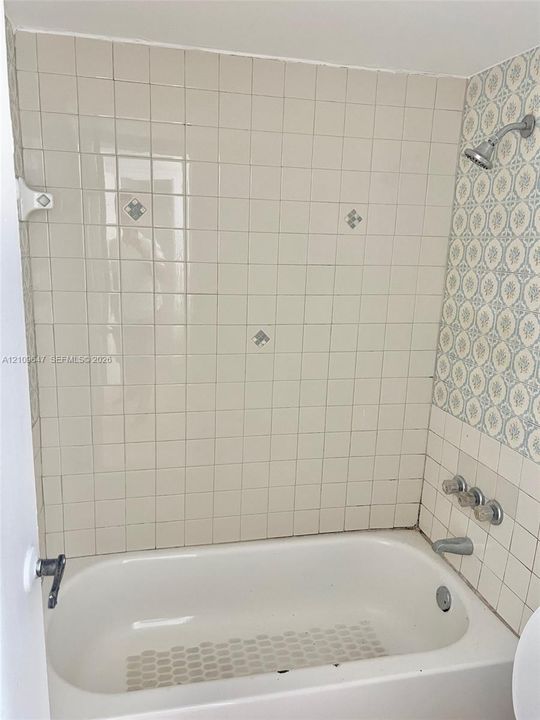 Bathtub enclosure featuring white ceramic wall tiles with decorative floral accents, integrated chrome shower head, and three-handle chrome faucet hardware
