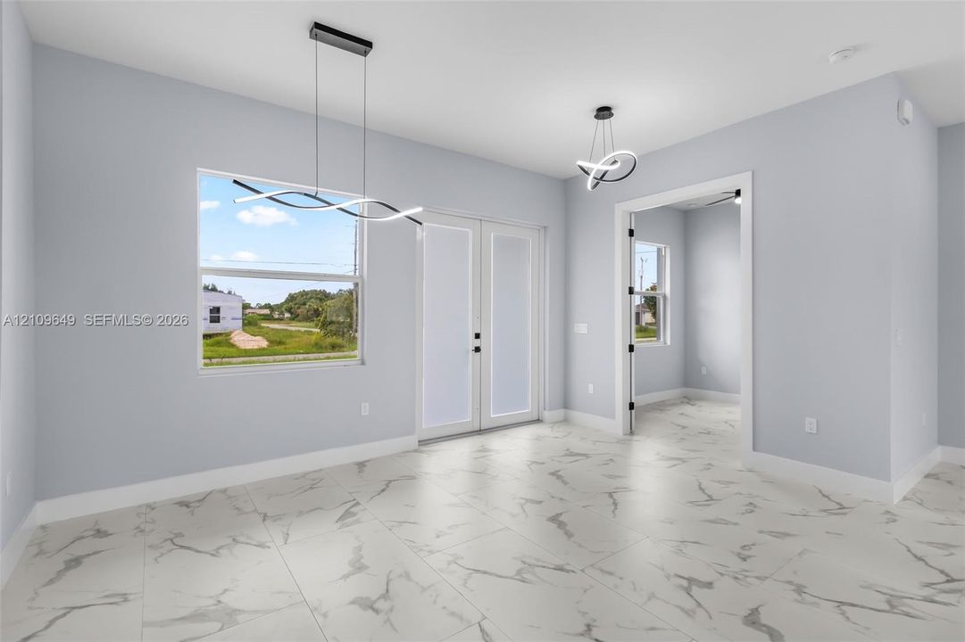 Large-format stone-finish flooring with veining detail, double-entry glass paneled doors, and contemporary sculptural overhead lighting fixtures