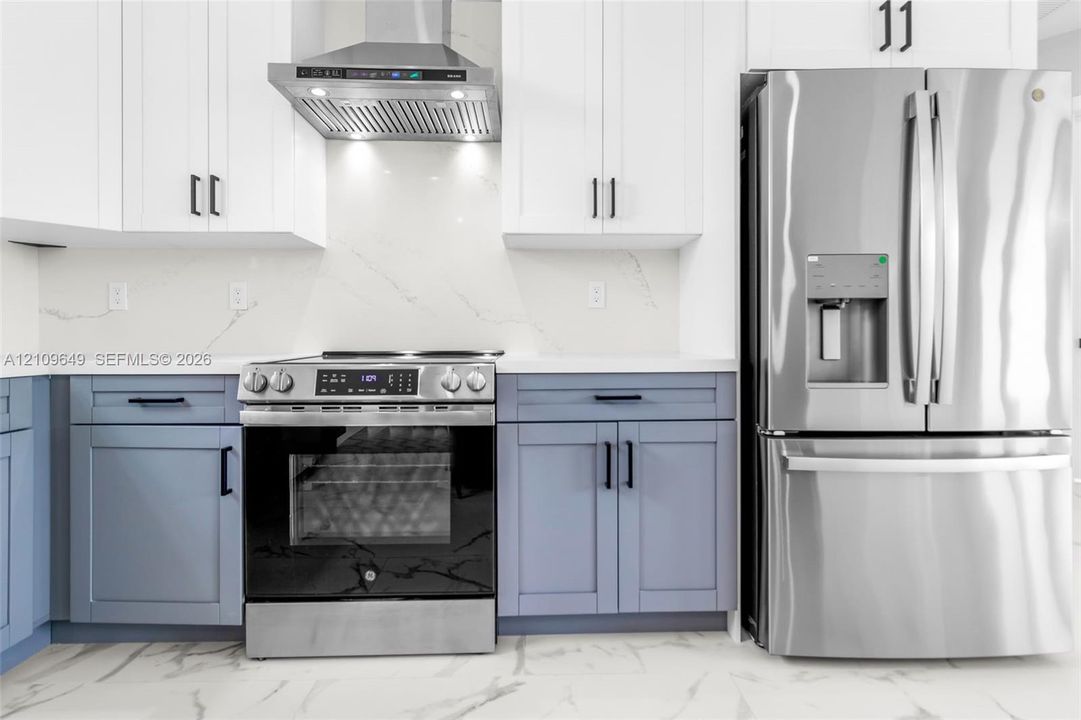 Kitchen featuring two-tone cabinetry with matte black hardware, stainless steel appliances, stone-look backsplash, and stone-look countertops