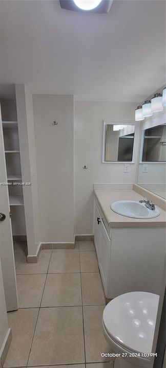 Vanity cabinet with integrated solid-surface countertop and drop-in basin, tiled flooring, wall-mounted mirror, built-in shelving unit, and multi-light fixture