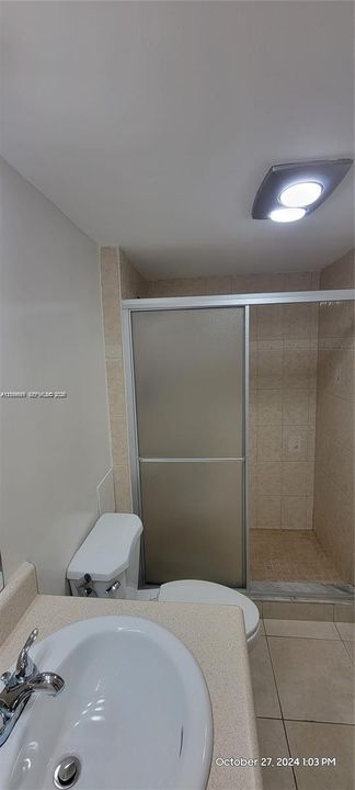 Bathroom featuring a vanity with an integrated basin, a walk-in shower with a sliding frosted glass door, tile wall surround, and ceiling-mounted flush light fixture