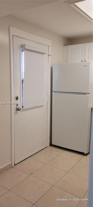 White top-mount refrigerator, neutral ceramic tile flooring, and exterior door with a vertical window insert