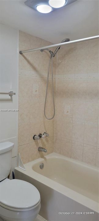 Bathtub and shower combination featuring neutral-toned wall tile, a handheld showerhead, chrome hardware, and an overhead flush-mount light fixture