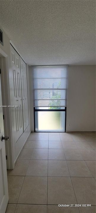 Neutral-toned tile flooring, floor-to-ceiling window with white roman shades, and built-in closet storage with paneled doors