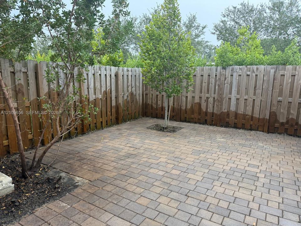 Paved patio featuring stone-finish interlocking pavers, wood privacy fencing, and mature trees