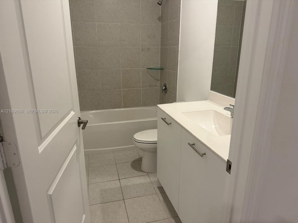 Bathroom featuring a white vanity with a composite countertop, an integrated rectangular sink, wall-to-wall mirror, and a tile-surround shower and tub combination