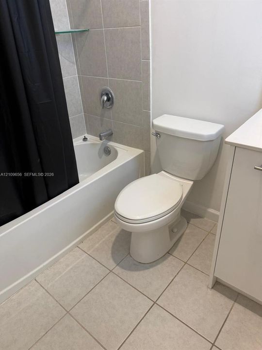 Bathroom featuring a tub-shower combination with ceramic tile surround, a built-in glass corner shelf, a white vanity, and ceramic tile flooring