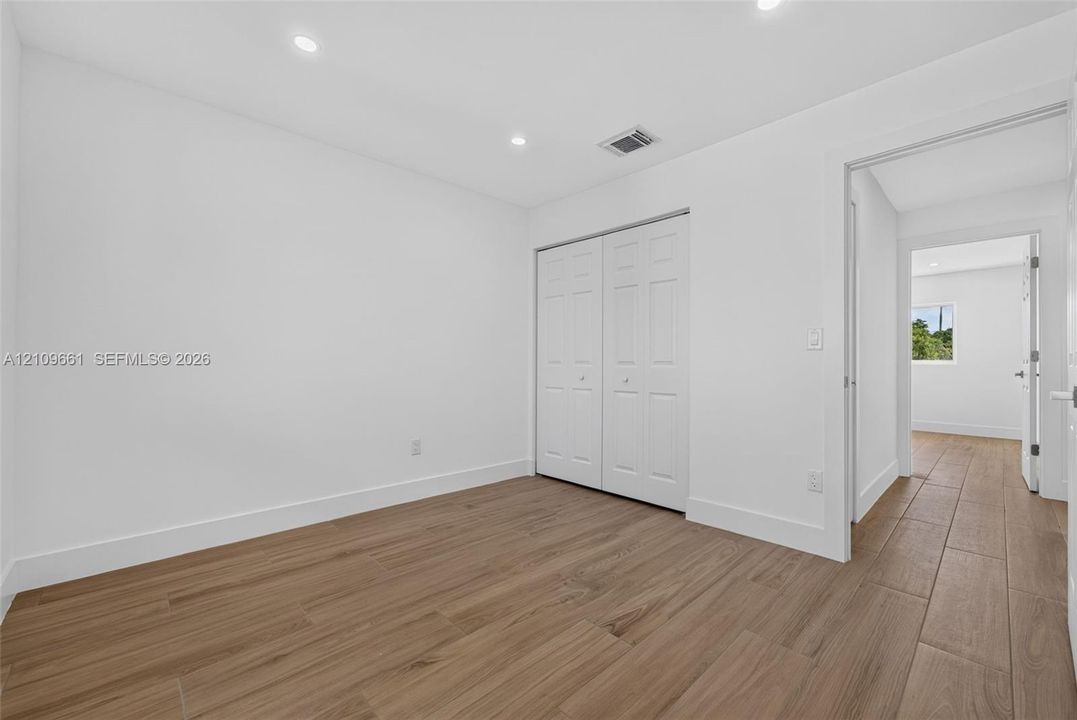 Neutral interior featuring wood-finish tile flooring, recessed ceiling lighting, and a double-door closet with paneled detailing