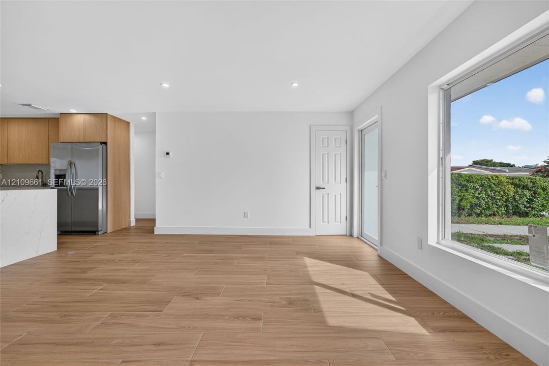 Open-concept kitchen featuring wood-finish cabinetry, a white countertop island, recessed lighting, wood-finish flooring, and a large exterior-facing window