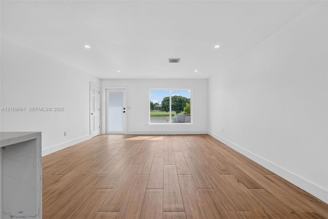 Open-concept room featuring wood-finish flooring, recessed lighting, a single-panel glass door, and a large window