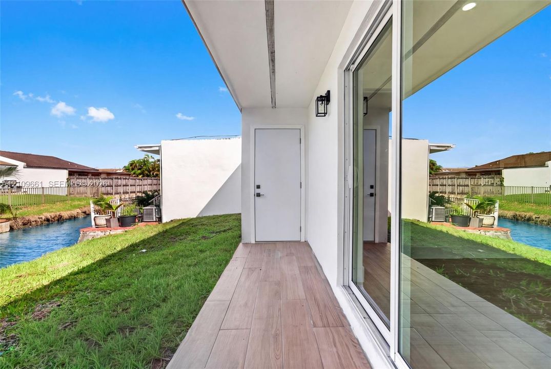 Covered patio featuring wood-finish tile flooring, sliding glass doors, and a solid exterior door, situated along a water feature