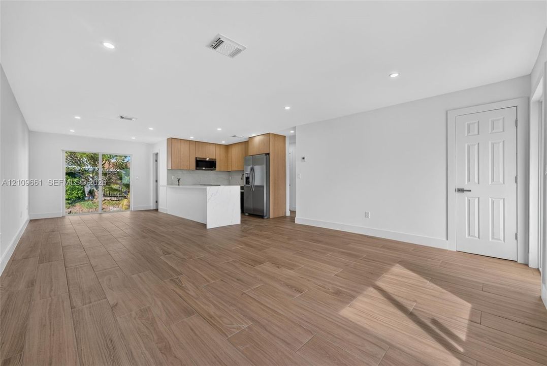 Open-concept interior featuring wood-finish flooring, recessed lighting, a center island with solid-surface countertops, light wood-finish cabinetry, and sliding glass doors