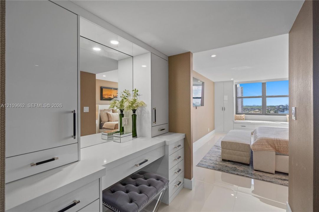Built-in vanity featuring high-gloss cabinetry, stone countertops, integrated mirror, and polished metal hardware