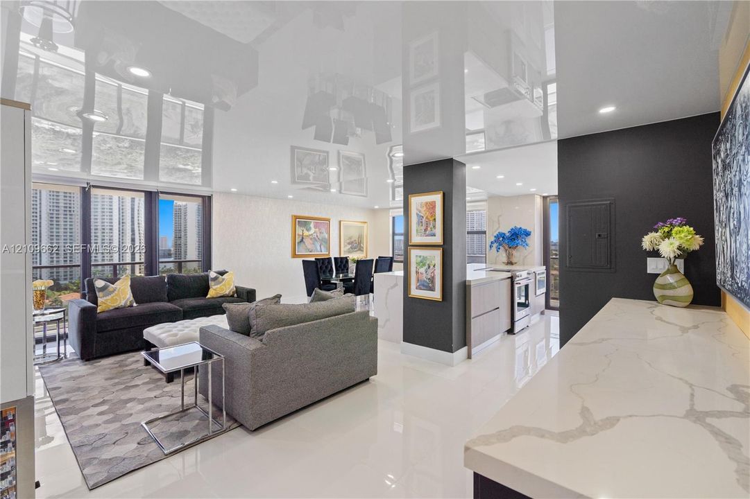 High-gloss reflective ceiling, stone countertop with waterfall edge, recessed lighting, floor-to-ceiling windows, and polished porcelain flooring