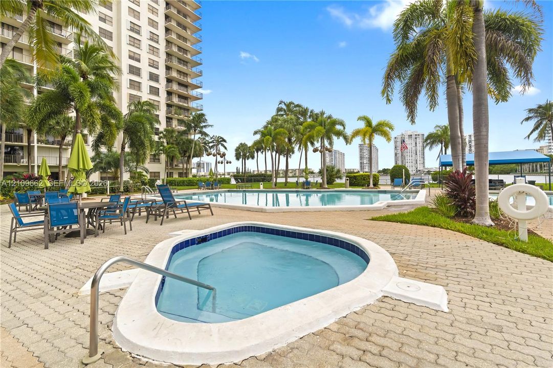 Outdoor pool and spa area featuring a paver deck, palm trees, and waterfront perimeter