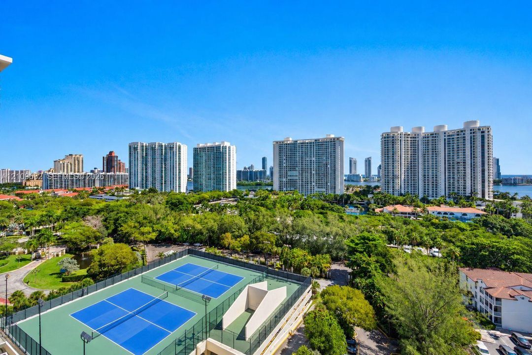 Dual tennis courts featuring hard-court surfaces and perimeter fencing, set against a backdrop of mature landscaping and high-rise development