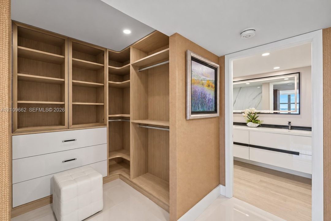 Custom walk-in closet featuring built-in wood-finish shelving, integrated clothing rods, and white drawer cabinetry, complemented by a dual-sink vanity with a backlit mirror and stone-surface countertop