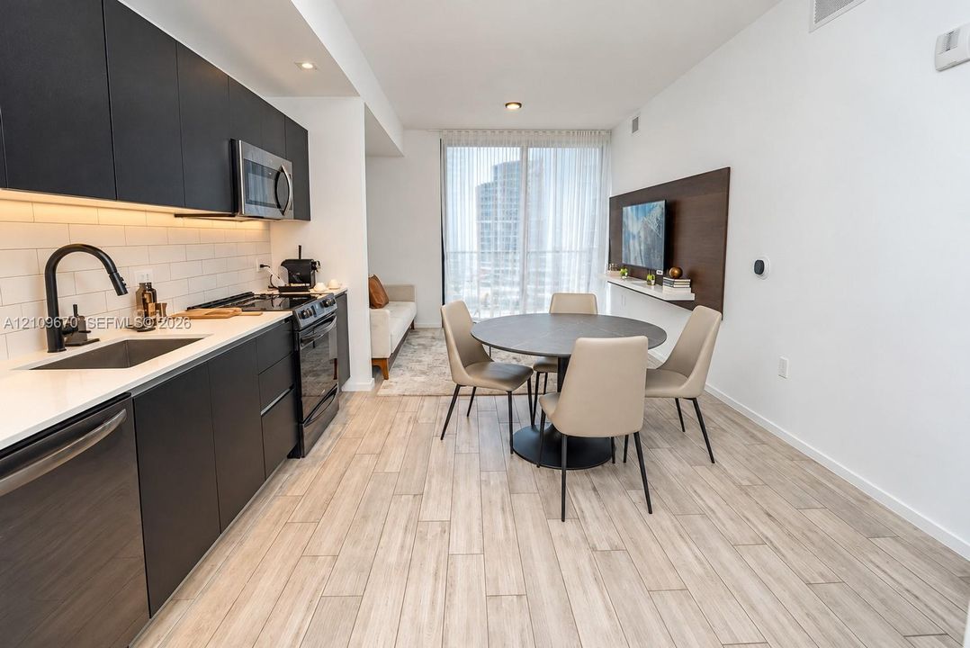 Kitchen featuring matte black flat-panel cabinetry, white quartz countertops, subway tile backsplash, and stainless steel appliances, complemented by light-toned wood-finish flooring