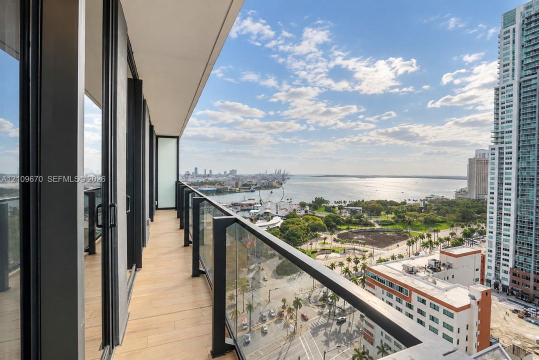 Covered balcony featuring wood-finish tile flooring, sleek black metal railings, and integrated glass panels