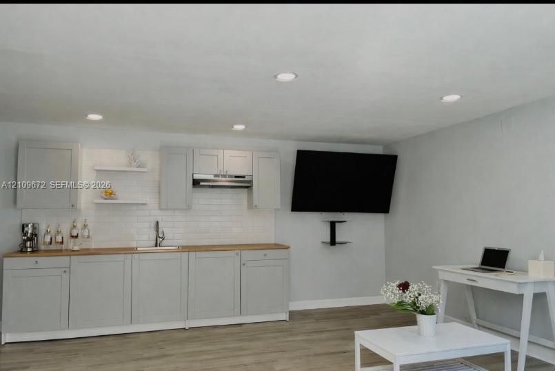 Light gray Shaker-style cabinetry, butcher block countertop, white subway tile backsplash, stainless steel under-mount sink with gooseneck faucet, and floating wall shelves