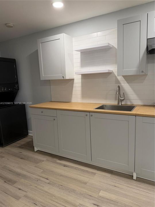 Stainless steel refrigerator, stacked washer and dryer, wood-finish flooring, and cabinetry with a light-toned countertop
