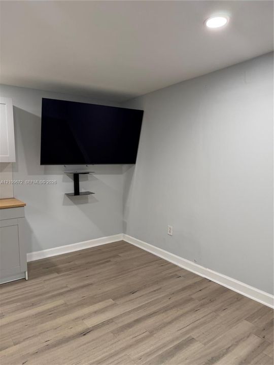 Light gray shaker-style cabinetry, wood-finish countertops, stainless steel sink, tile backsplash, and wood-finish flooring