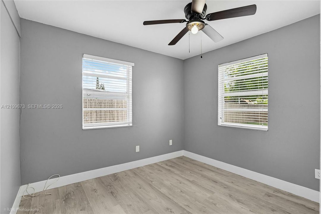Interior space featuring wood-finish flooring, neutral gray wall paint, dual windows with horizontal blinds, and a central ceiling fan with an integrated light fixture