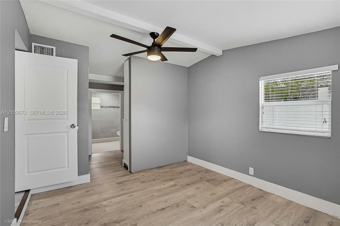 Interior space featuring wood-finish flooring, neutral-toned walls, a white multi-panel interior door, and a ceiling fan with integrated lighting