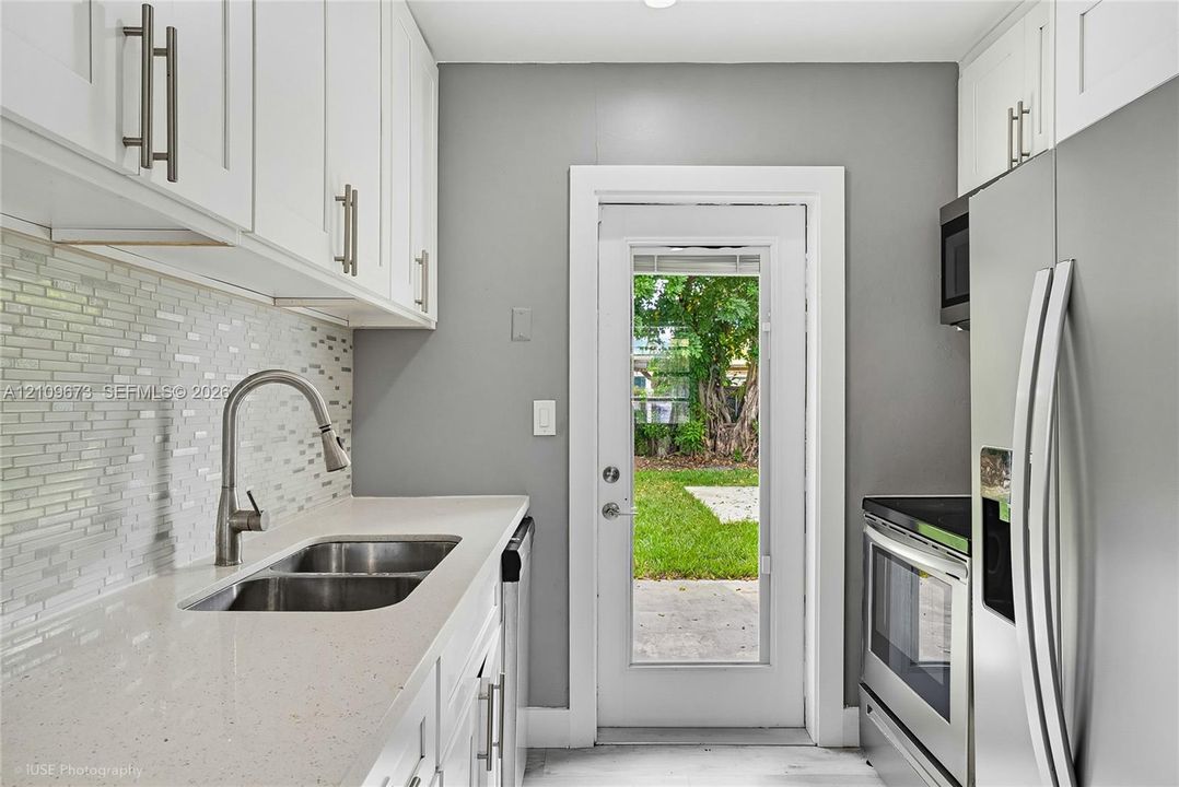 Kitchen featuring white cabinetry, solid-surface countertops, mosaic tile backsplash, stainless steel appliances, and a glass-panel exterior door