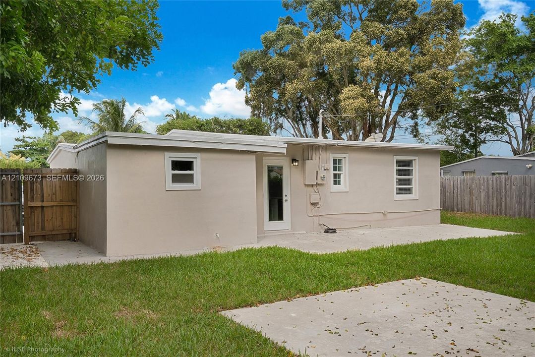 Exterior rear elevation featuring a concrete patio, stucco siding, multi-lite windows, and a wood privacy fence
