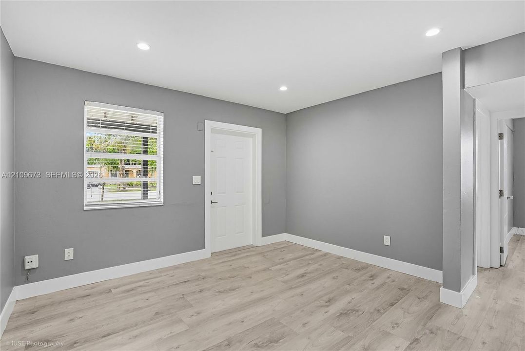 Neutral gray wall paint, light-toned wood-finish flooring, recessed ceiling lighting, and a window with horizontal blinds