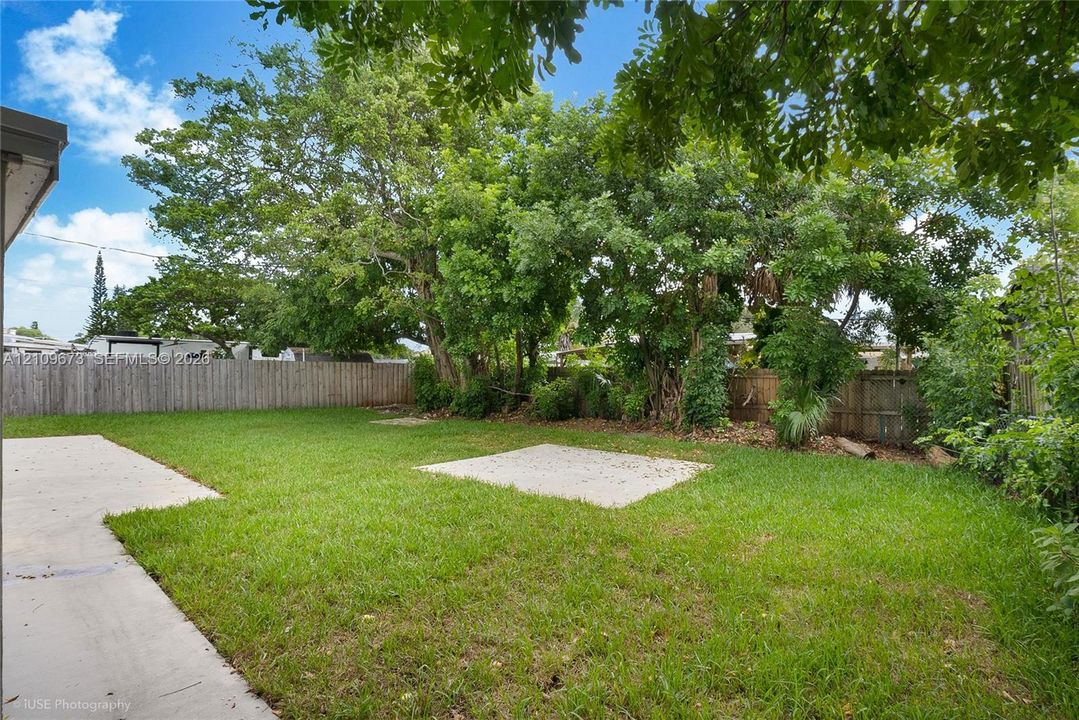 Private backyard featuring a concrete patio, grassy lawn, wood privacy fencing, and mature trees