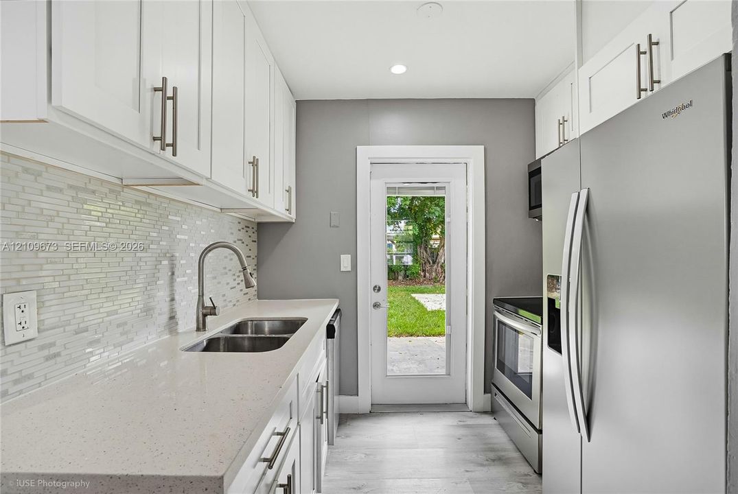 Kitchen featuring white shaker-style cabinetry, solid-surface countertops, a mosaic tile backsplash, stainless steel appliances, and wood-finish flooring