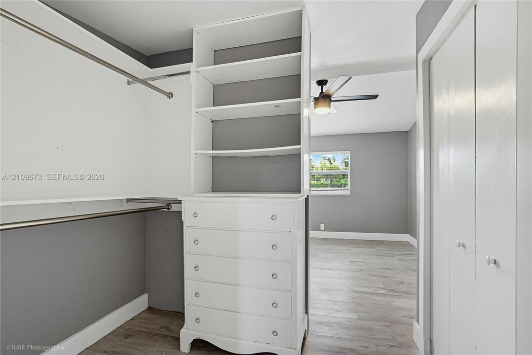 Walk-in closet featuring built-in white cabinetry with open shelving and drawers, wood-finish flooring, and dual hanging rods
