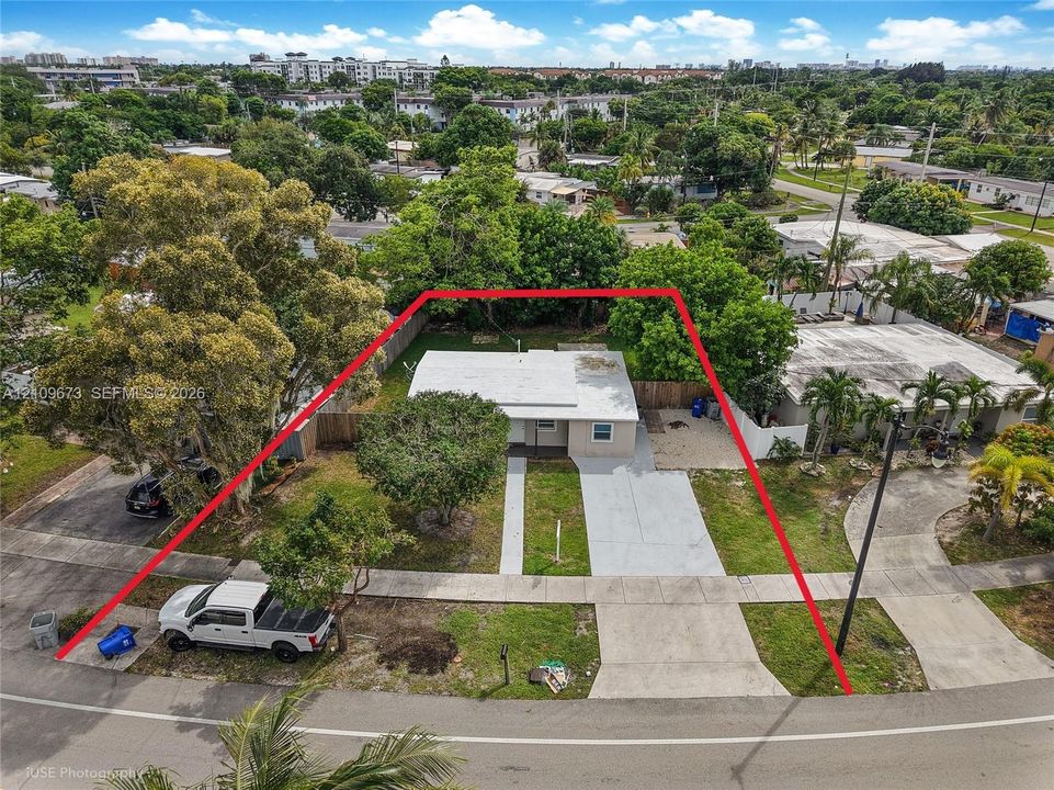 Single-story residence featuring a flat roof, concrete driveway, fenced perimeter, and established tree canopy on a rectangular lot