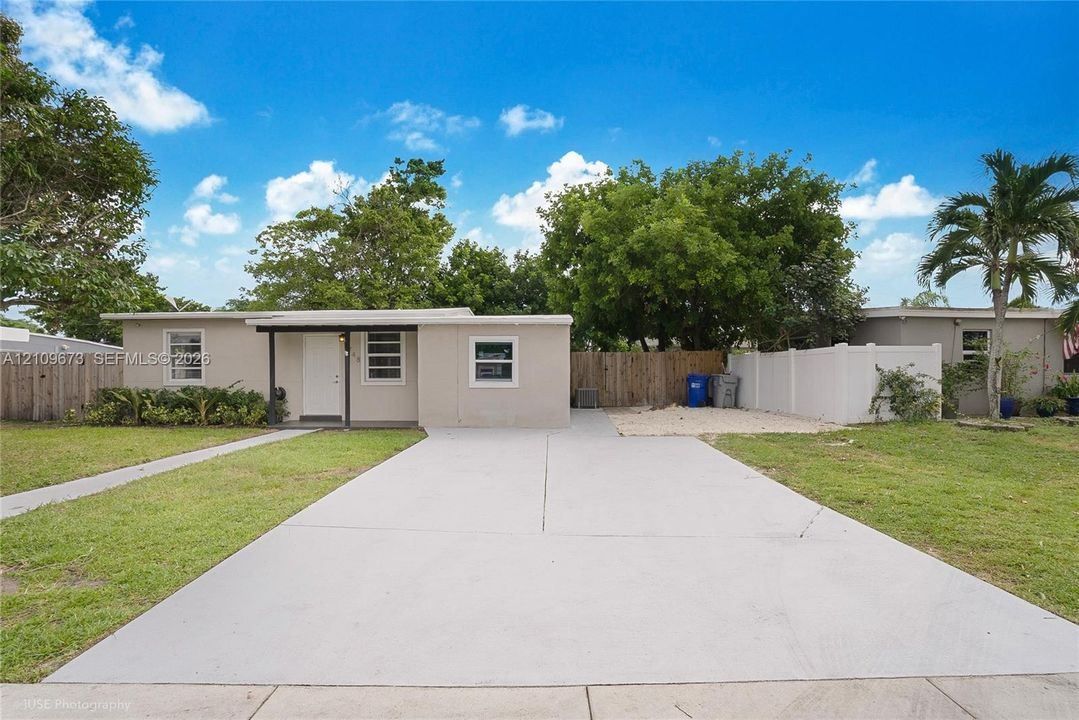 Single-story exterior featuring a concrete driveway, covered front entryway, horizontal sliding windows, and perimeter privacy fencing