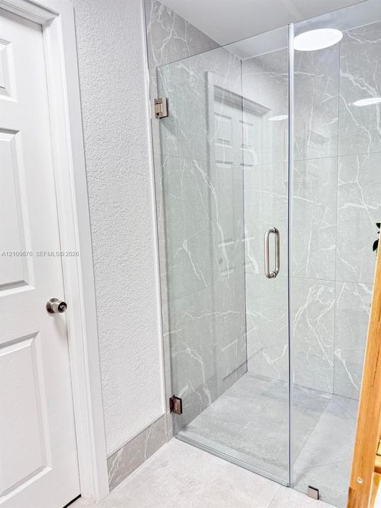 Walk-in shower with floor-to-ceiling large-format stone-finish wall tiles, frameless glass enclosure, and metallic hardware