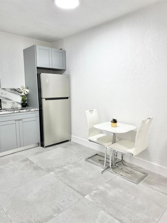 Shaker-style cabinetry with neutral finish, stone-patterned countertops, stainless steel refrigerator, and large-format tile flooring