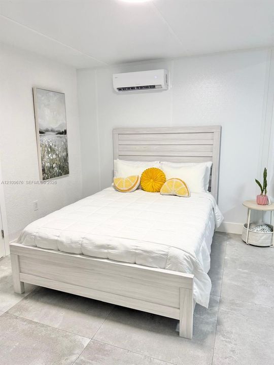 Neutral-toned interior featuring large-format tile flooring, white wall finishes, and a wall-mounted ductless climate control unit