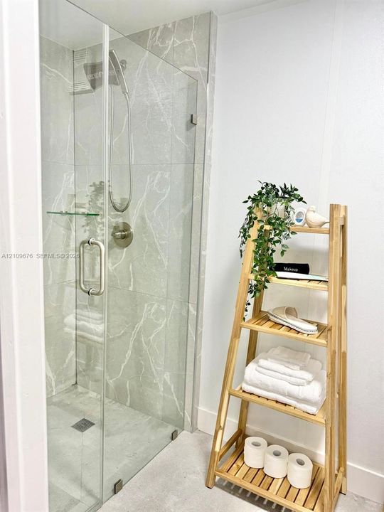 Walk-in shower featuring large-format patterned wall tile, frameless glass door, brushed nickel hardware, and an integrated glass shelf