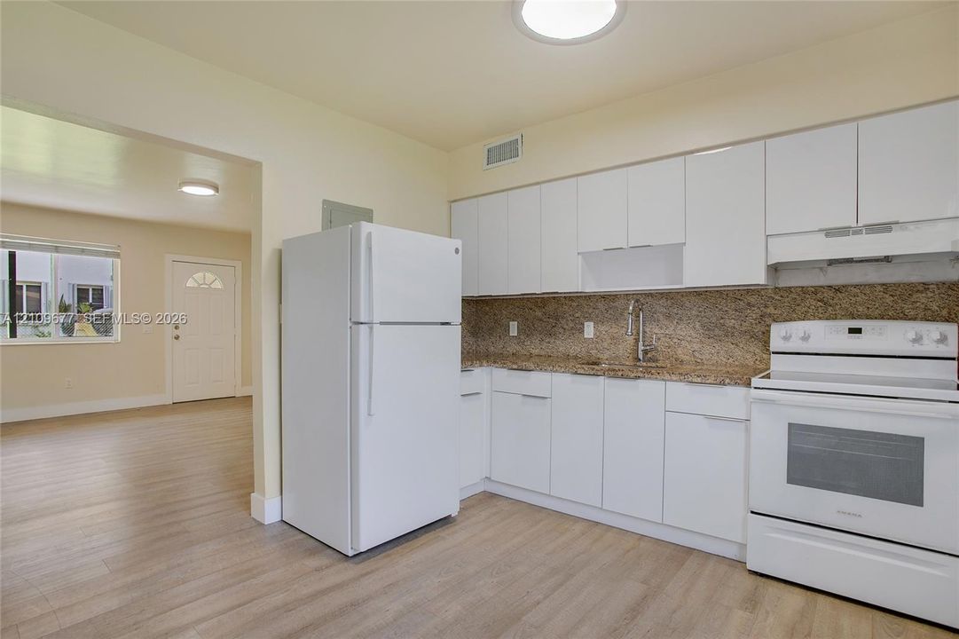 Kitchen featuring white cabinetry, stone-finish countertops, and matching white appliances including a refrigerator and range, complemented by wood-finish flooring