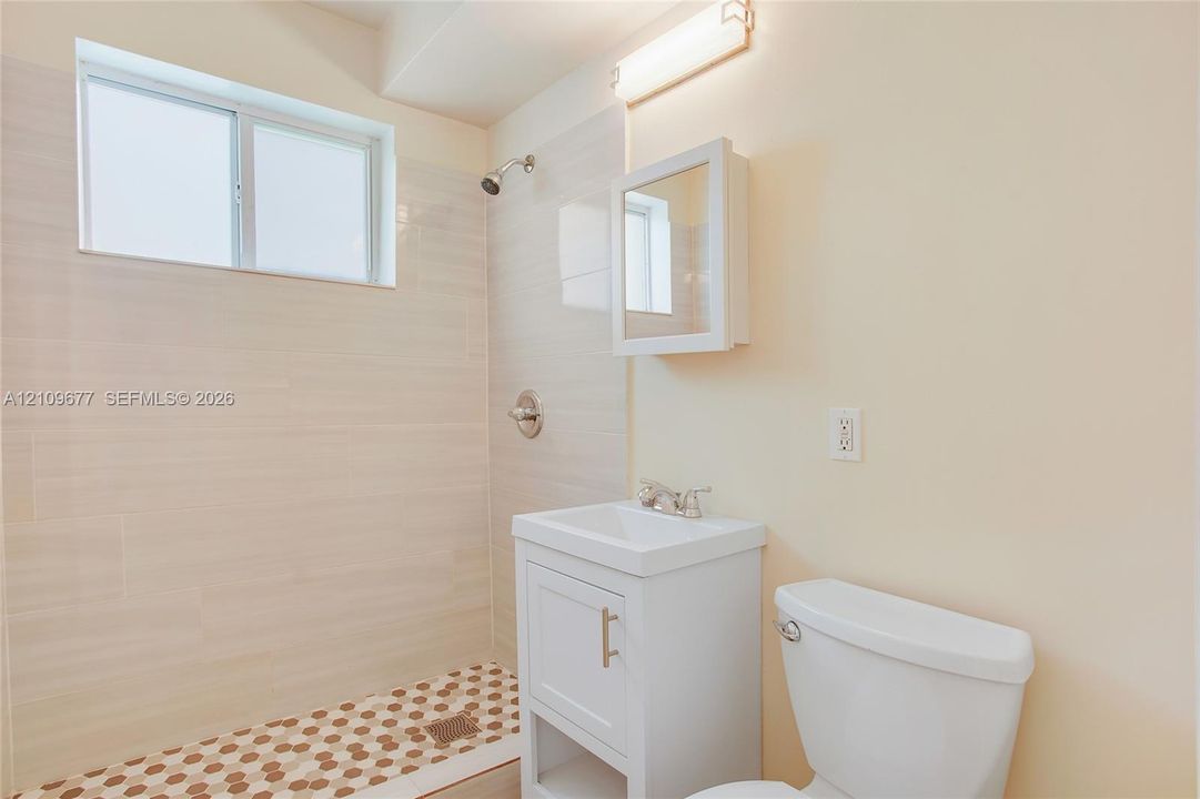 Bathroom featuring a white vanity cabinet, square porcelain sink, wall-mounted medicine cabinet, horizontal shower tile surround, and patterned mosaic tile flooring