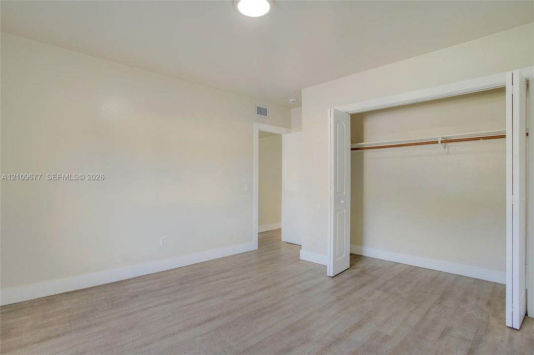 Neutral-toned interior space featuring light wood-finish flooring, smooth wall surfaces, and a walk-in closet with integrated shelving
