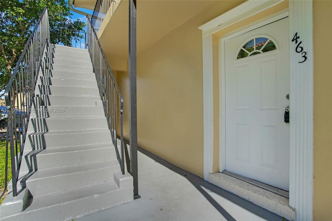 Exterior entrance featuring a white panel door with an arched glass insert, fluted trim surround, concrete staircase, and black metal handrailing